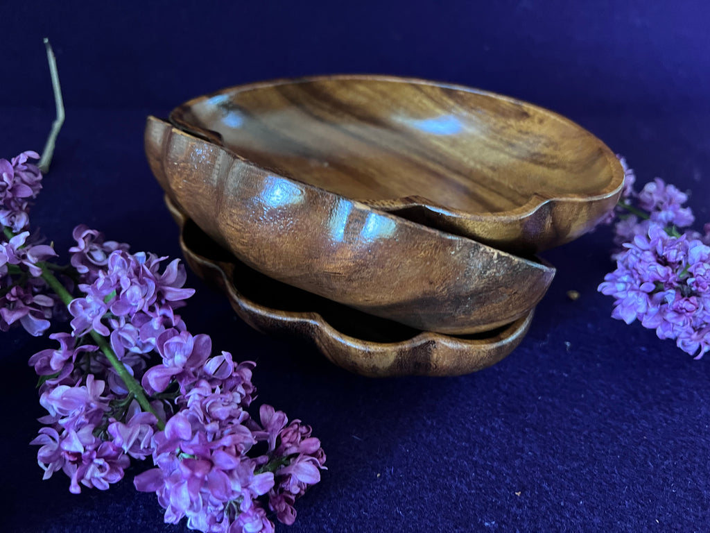 Wooden bowl with a textured surface on a dark background with purple flowers.